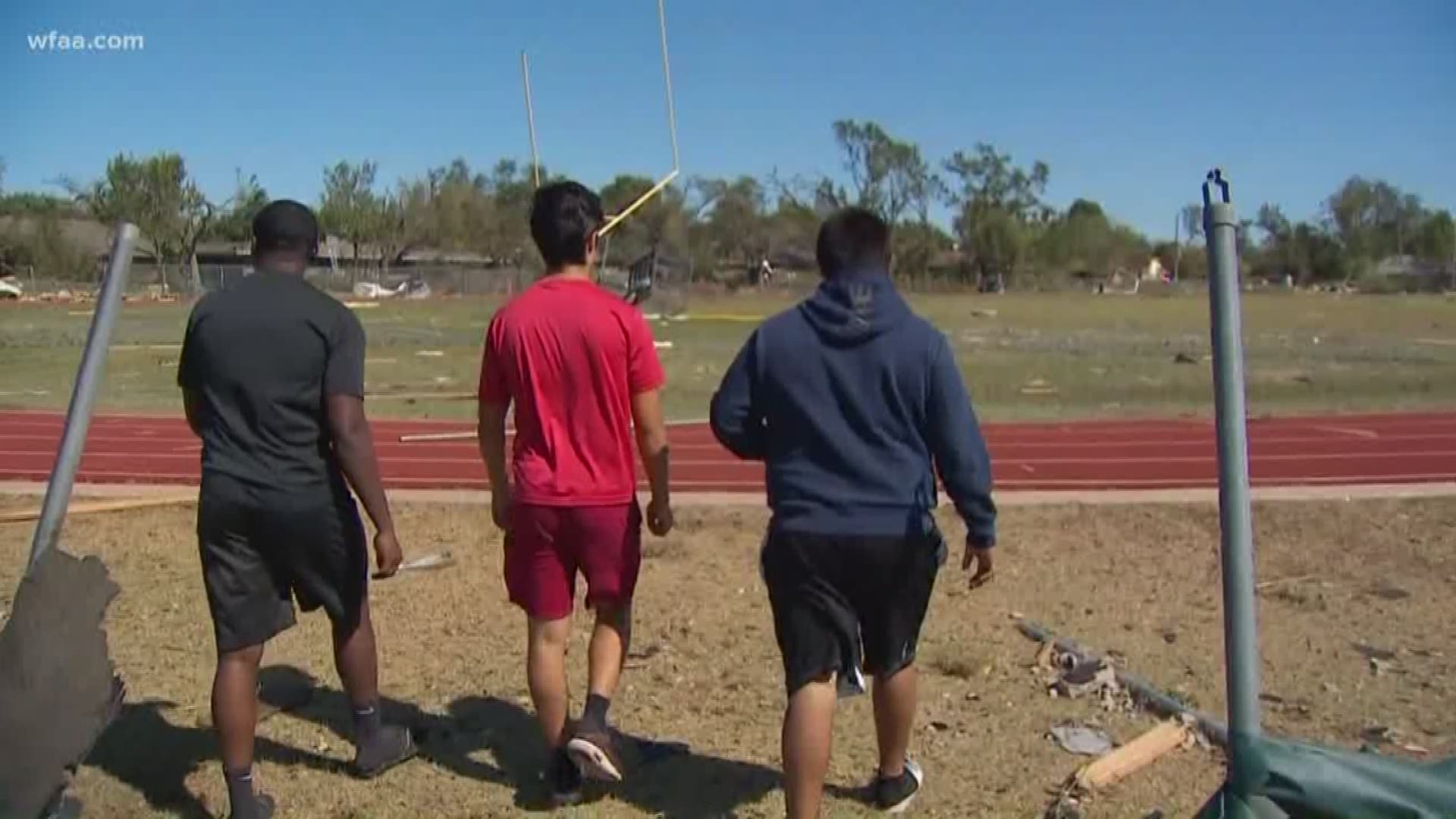 Three seniors at a high school in Dallas, Texas walk their school grounds past destruction after a tornado devastated their campus.